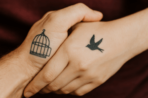 Zwei Hände: auf einer ist eine Taube und auf anderen ein offener Vogelkäfig tätowiert. Ein Symbolbild für Traubindung.