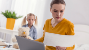 Eine beschäftige Frau mit ihrer kleiner Tochter im Hintergrund, als Symbolbild für Mutterwunde durch emotionale Vernachlässigung in der Kindheit