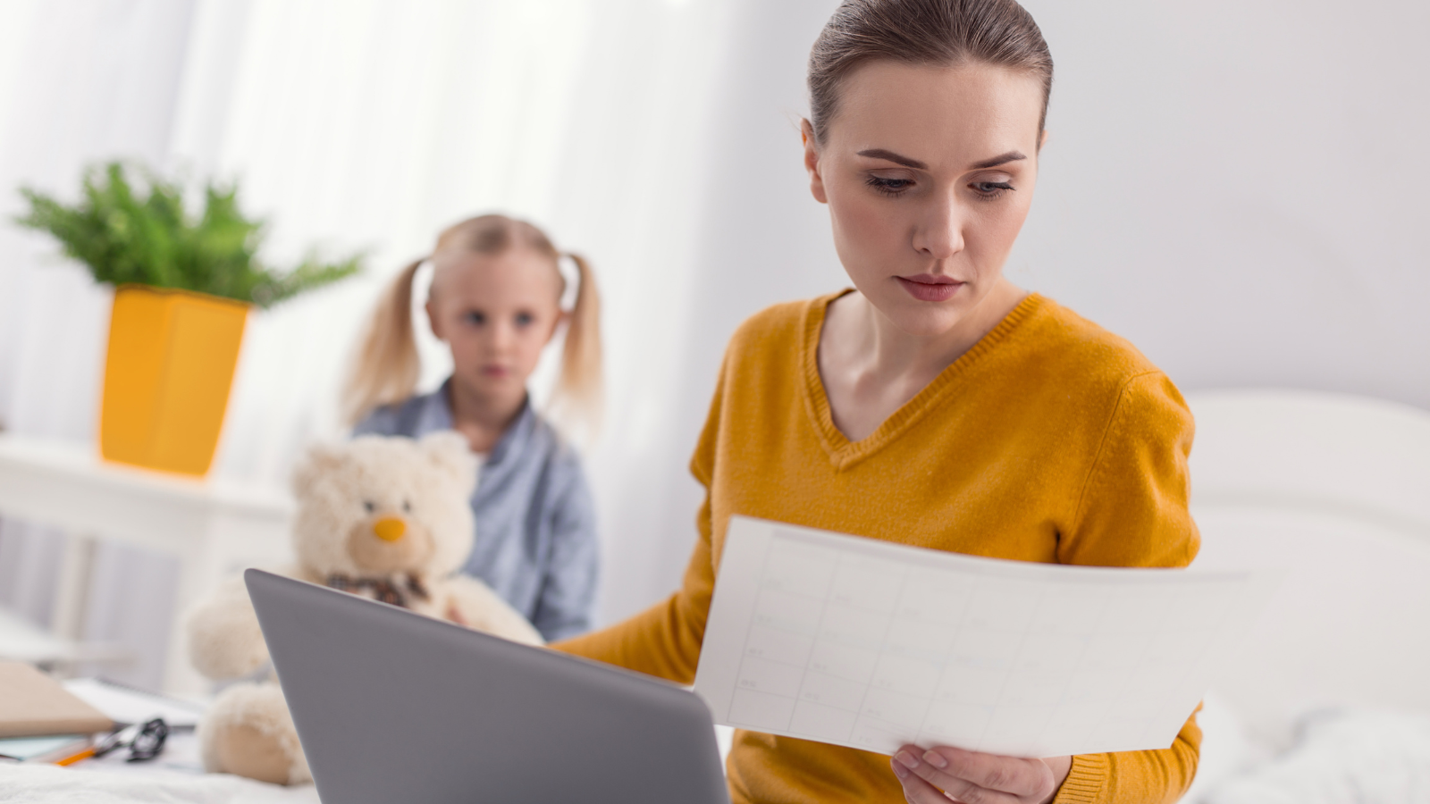 Eine beschäftige Frau mit ihrer kleiner Tochter im Hintergrund, als Symbolbild für Mutterwunde durch emotionale Vernachlässigung in der Kindheit